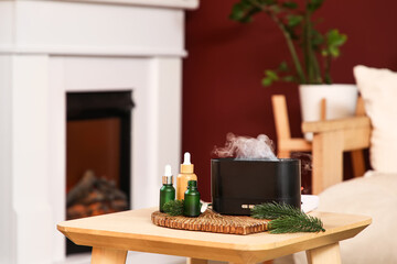 Aroma diffuser with essential oils and fir branches on table in living room