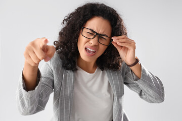 Angry African-American businesswoman pointing at viewer on light background