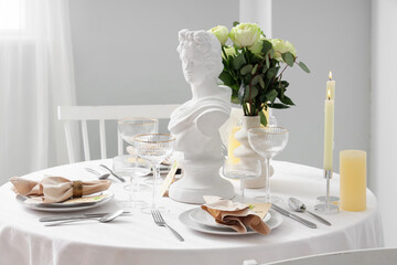 Table setting for Nobel prize day with Greek statuette and roses in light room
