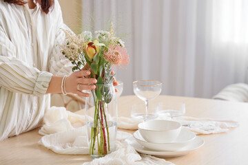 Young woman serving table with beautiful flowers in dining room