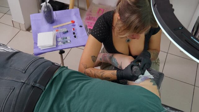 Female tattoo artist working on a client's leg in a studio