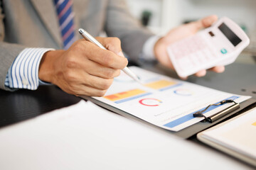 A man is using a calculator to add numbers. He is wearing a suit and tie. Concept of professionalism and focus