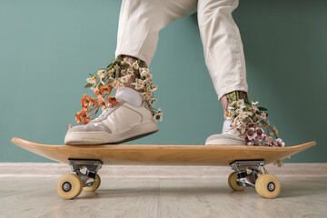 Female legs with flowers and skateboard near turquoise wall