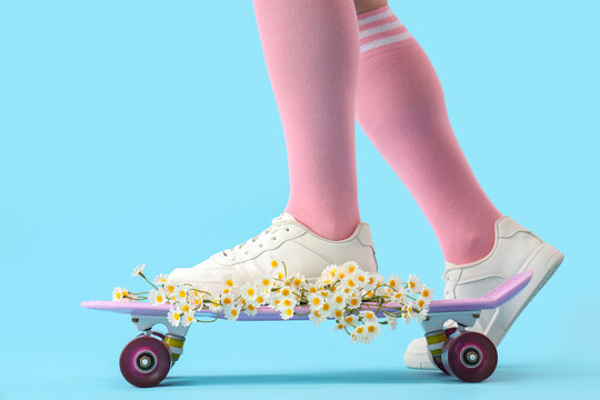 Female legs with daisies and skateboard on blue background - Powered by Adobe