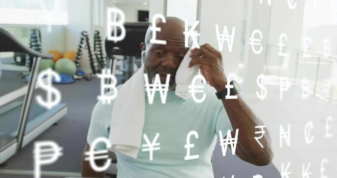 Mature man ending workout grabbing towel dabbing face exhaling amid currency symbols over frame
