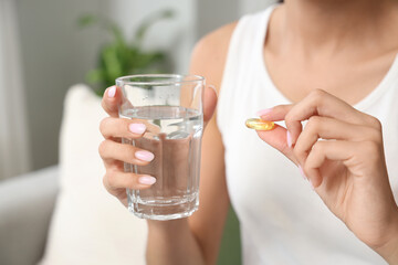 Young woman with vitamin E pill and glass of water at home, closeup