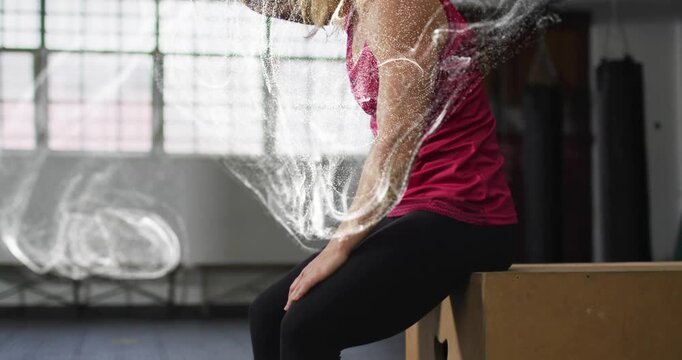 Female athlete on plyo box rubbing hands and making chalk cloud wrapping arms preparing for workout