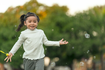 happy toddler girl running and playing soap bubble in park