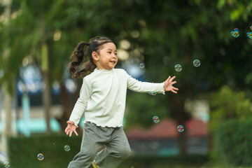 happy toddler girl running and playing soap bubble in park