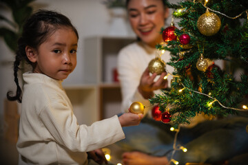 mother and toddler girl decorating Christmas tree in home at night