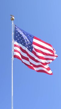 Verti al screen american flag waving against clear sky johnson city park flagpole with gold finial, bright midday sunlight, gentle breeze causing flowing stars and stripes, vivid red white