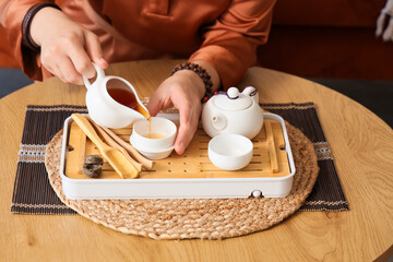 Asian woman pouring tea on table at home, closeup