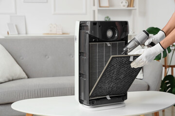 Female technician with handheld vacuum cleaner cleaning dirty air purifier filter at home
