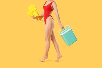 Young woman in swimsuit, with swimming flippers and portable fridge on yellow background © Pixel-Shot