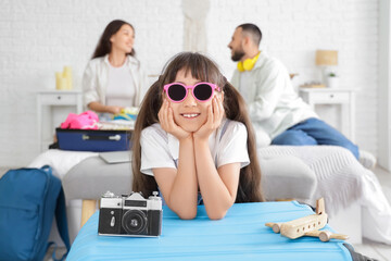 Cute girl against her parents packing suitcase in bedroom