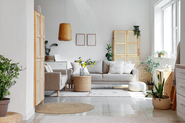 Comfortable beige sofas, wicker table and houseplants in interior of living room