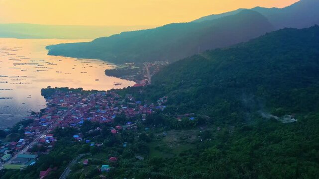 A descending aerial of golden sunset over Talisay and Taal Lake fading into winding forest road in Batangas, Philippines