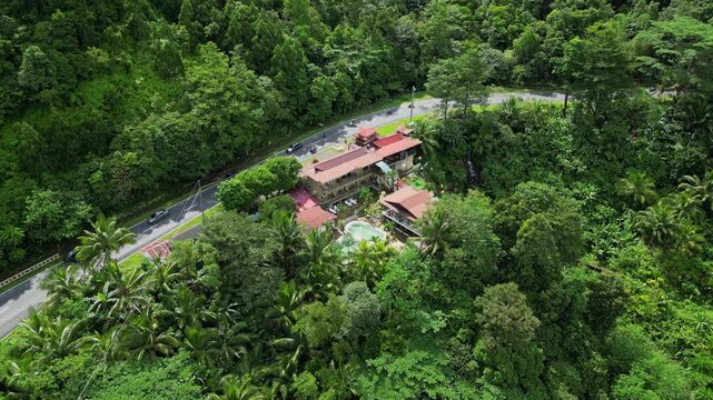 Forward aerial of resort hotel with red roofs and pool nestled in tropical forest beside Marcos Highway in Tanay Rizal.