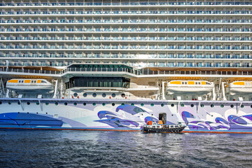 Obraz premium A tender boat pulls up next to a large cruise ship as it prepares to take passengers from the sea to the port.