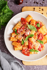 Plate of delicious penne pasta with tomato and basil on grunge background
