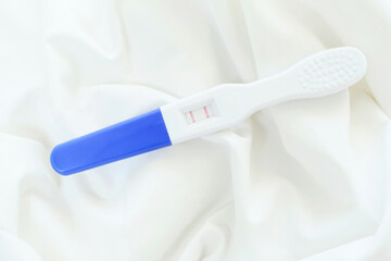 Positive pregnancy test with two stripes on white background, top view.