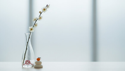 ガラス花瓶の白い梅の花と鏡餅飾りと水引のミニマルなお正月イメージ