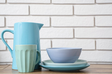 Stack of blue clean tableware on wooden table near white brick wall