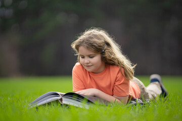 Naklejka premium Kid read a book in the grass. Kid read a book story outdoors. Kid read book in the meadow on a sunny day. Reading in nature. Schoolboy with book. Kid outdoor learning. Kids read story.