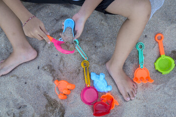 A faceless photo showing a small child playing in the sand using colorful tools.