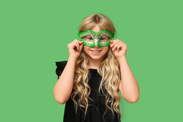 Funny little girl wearing carnival mask on green background