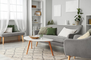 Interior of light living room with grey sofa, table and armchair