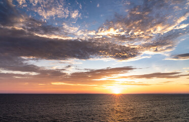 Sun rises above the horizon, casting sunbeams of light over the sea. Waves gently move in the Skagerrak sea Sweden. Orange and yellow colors fill the sky during the golden hour. Camera angle tilt up