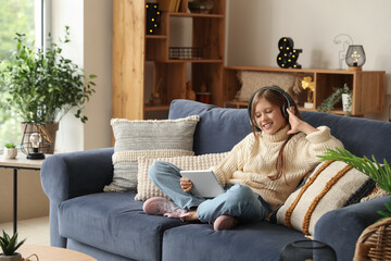 Little girl in headphones using tablet computer at home