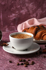 Cup of delicious espresso with coffee beans and croissant on purple background