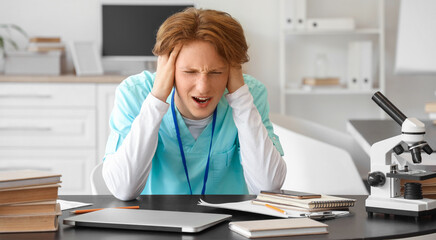 Stressed male medical intern studying at table in clinic