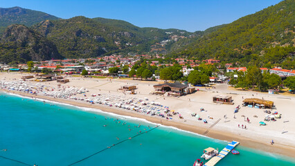Oludeniz, Turkey. Aerial view of Oludeniz Beach from water, people on sunbeds, wooden pier, umbrellas and turquoise sea with white foam waves, summer.. Aerial View