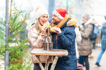 Couple eating sausages and fresh rolls at a Christmas market enjoying cozy winter flavors and festive lights