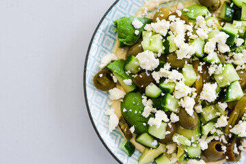 healthy nourish bowl with avocado, jalapeno, feta, green olives and cucumber on hummus