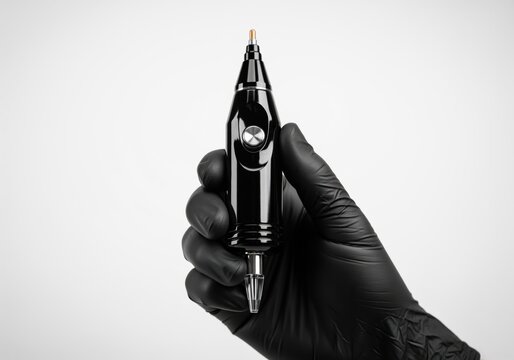 Professional black rotary tattoo machine pen held by an artist wearing a protective black glove.