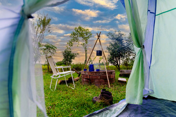 Looking out from the inside of the tent, resting equipment for setting up a camping tent in the forest in the morning, camping tents with outdoor coffee-making facilities