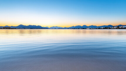 Calm lake sunrise with distant mountain silhouette and pastel sky
