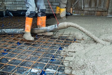 A construction worker pours concrete for a slab with reinforcement mesh. This image highlights the...