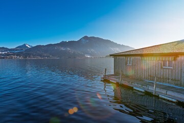 Experience lakeside tranquility with a rustic cabin by the water, surrounded by mountains under a clear sky. Perfect for travel, vacation, or real estate themes.