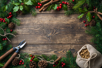 A festive frame of evergreen boughs, holly, cinnamon, and pinecones on a rustic wood background. Ideal for Christmas craft, DIY decor, and natural winter border concepts. copy space