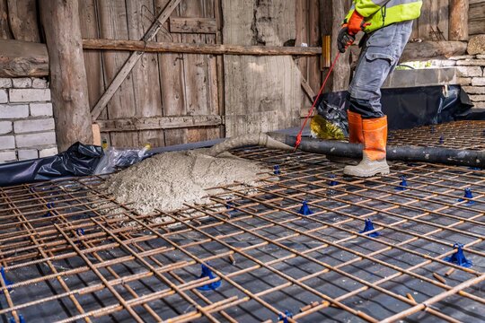 A groundworker skillfully pours concrete onto a metal grid at a construction site. This image highlights the crucial step of laying a solid foundation for building projects.