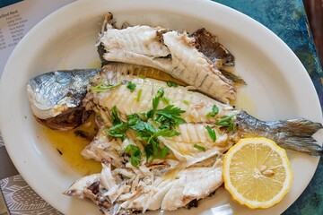 A whole grilled fish is served on a white plate, garnished with fresh parsley and a slice of lemon. This dish exemplifies healthy seafood cuisine for menus and food blogs.