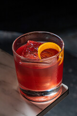 A vibrant cocktail filled with ice glimmers in the dim light, showcasing a twist of orange
