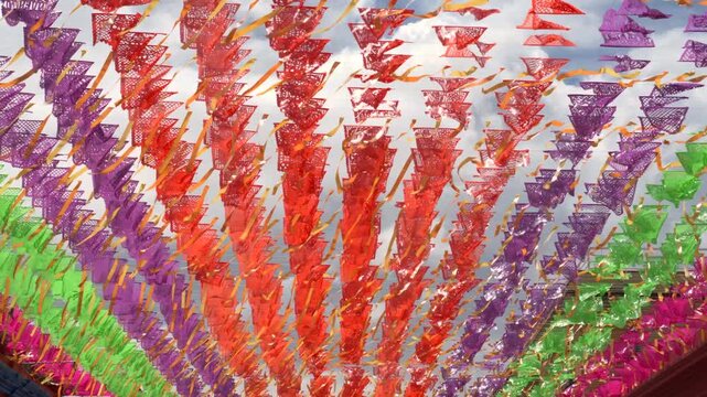 Papel picado rows sway across open market walkway creating colorful patterned canopy overhead, textured beautiful backdrop