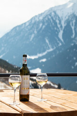 Fototapeta premium Osh, Kyrgyzstan - December 13, 2024: A bottle of Atalyk white wine and two glasses stand on a wooden table with a dramatic, snowy, mountainous background