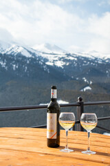 Fototapeta premium Osh, Kyrgyzstan - December 13, 2024: A bottle of Atalyk white wine and two glasses stand on a wooden table on a terrace overlooking vast, snow-covered mountains